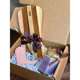 Boot Board Gift Box with wooden boot-shaped board, jar of honey with spoon, pink boot soap, and spreader tied with ribbon in kraft box