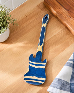 Blue and beige spatula on a wooden surface with a plant and towel in the background