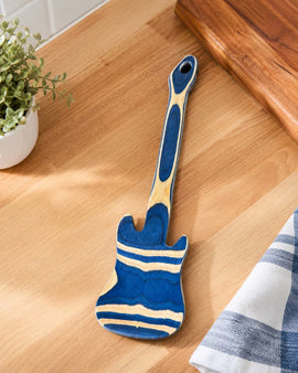 Blue and beige spatula on a wooden surface with a plant and towel in the background