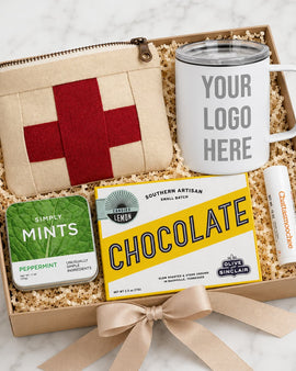 Gift set with mug, pouch, mints, and chocolate bar in a box on a marble surface.