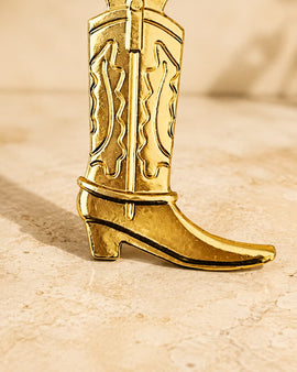 Gold cowboy boot bottle opener on a beige background
