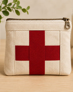 Small beige pouch with a red cross on a wooden surface