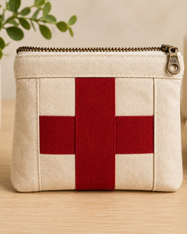 Small beige pouch with a red cross on a wooden surface