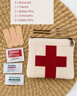 First aid kit with band-aids, Tylenol, bobby pins, and ointments on a woven mat.