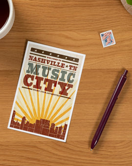 Poster with 'Welcome to Nashville, TN Music City' text on a wooden surface with a pen and coffee cup.