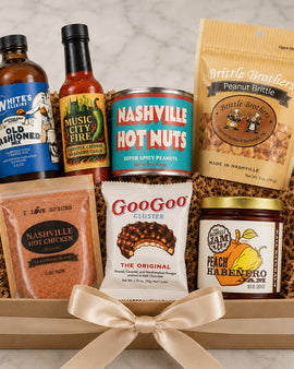 Assorted gift set with hot sauce, snack items, and a jar of jam in a box.