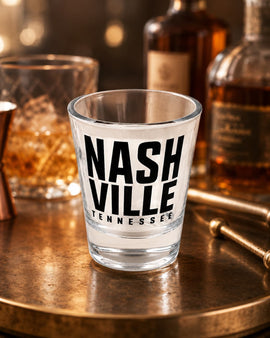 Clear shot glass with 'Nashville Tennessee' text on a bar counter with bottles in the background